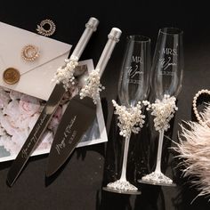 two champagne flutes, one with pearls and the other decorated with flowers are sitting next to an envelope