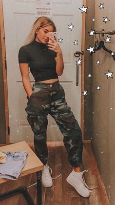 a woman in black shirt and camo pants standing next to door with stars on it