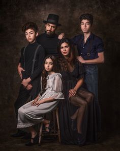 a group of people posing for a photo in front of a dark background with one woman sitting on a chair