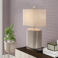 a lamp on a table next to a plant and books in front of a purple wall