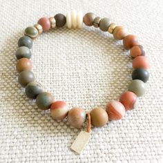 Picasso jasper raw semi-precious round stone bracelet. Colors range from neutrals to olives and grays. Features brass and bone details. Sterling silver BelleStyle logo tag. Comes in linen travel pouch. Made in USA. Earthy Natural Stones Beaded Bracelets, Earthy Jasper Beaded Bracelets With Natural Stones, Earthy Beaded Bracelets With Natural Jasper Stones, Earthy Jasper Beaded Bracelet With Natural Stones, Earthy Beige Jewelry For Everyday Wear, Earthy Everyday Beige Jewelry, Bracelet Colors, Picasso Jasper, Jasper Bracelet