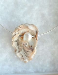 a necklace with a pearl in the center on a silver chain hanging from a white surface