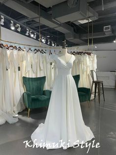 a white wedding dress is on display in a room with green chairs and other dresses