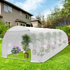 a greenhouse with plants growing inside it on the grass in front of a large house