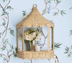 a basket with flowers in it on a shelf next to a wallpapered wall