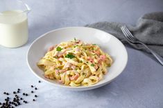 a white bowl filled with pasta and garnished with parsley next to a glass of milk