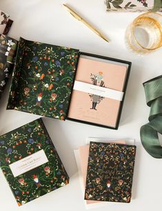 three notebooks with floral designs are sitting on a table next to some wrapping paper