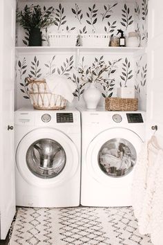 a white washer and dryer sitting in a room next to each other with leaves on the wall