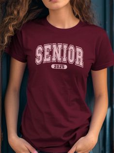 🌟 Stand Out in Your Senior Year with Our Vibrant Collegiate T-Shirt! 🌟 Get ready to celebrate your senior year with style and confidence with our eye-catching Senior Year T-Shirt in Cardinal Red! This design features the word "SENIOR" in large, blocky, and bold Collegiate letters, reminiscent of collegiate and varsity styles, perfect for making a statement. Below "SENIOR," the year "2025" is displayed in a similar bold font within an oval shape, adding a distinctive touch. The entire text and College Style Crew Neck T-shirt For College Events, Graphic Tee With Crew Neck For College Events, Collegiate Short Sleeve Tops For College Events, Text Print Crew Neck Top For College Events, Graphic Tee Crew Neck For Graduation, Letter Design, School Events, Pink Tshirt, Senior Year