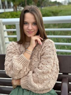 a woman is sitting on a bench with her hand under her chin and looking at the camera