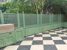 an outdoor kitchen area with checkered tile flooring and green fenced in grills