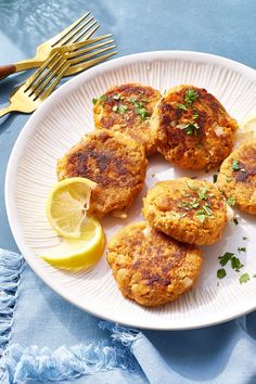 several crab cakes on a plate with lemon wedges