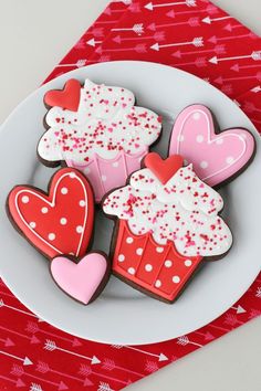 three decorated cookies on a white plate with red and pink hearts in the middle, sitting next to each other