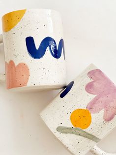 two coffee mugs with painted designs on them