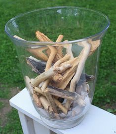 a glass vase filled with sticks and wood on top of a white wooden table outside