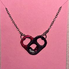 a black and red heart shaped pendant on a pink card with chain hanging from it