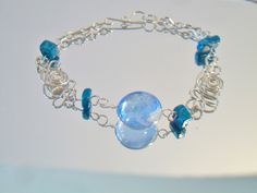 Blue beaded wire bracelet. It measures approx. 7 inches long and has a hook closure. Made with a round cornflower blue glass cabochon in the center, 4 deep turquoise blue glass square beads and swirling Peruvian Alpaca Silver wire chain. Handmade, delicate and light weight. Add it to your jewelry wardrobe. All sales are final and as is. Thank you for looking. You may also love this: https://www.etsy.com/listing/236165636/red-murano-glass-tear-drop-earrings-hoop?ga_search_query=murano&ref=sho Modern Turquoise Glass Jewelry, Blue Wire Wrapped Bracelets With Round Beads, Blue Wire Wrapped Bracelet With Round Beads, Turquoise Czech Glass Round Jewelry, Czech Glass Bracelet With Lobster Clasp, Blue Wire Wrapped Bracelets, Blue Glass Bracelet Jewelry, Unique Blue Wire-wrapped Bracelets, Turquoise Glass Round Jewelry