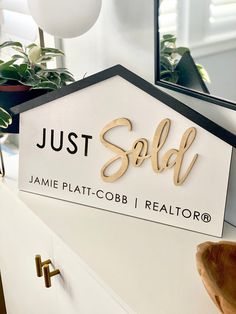 a white sign that says just sold on it next to a mirror and potted plant