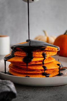 a stack of pancakes with chocolate drizzled on top and pumpkins in the background