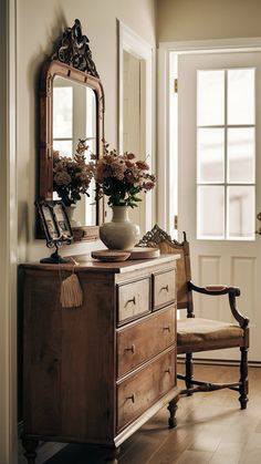 a vase with flowers on top of a dresser next to a mirror and chair in a room