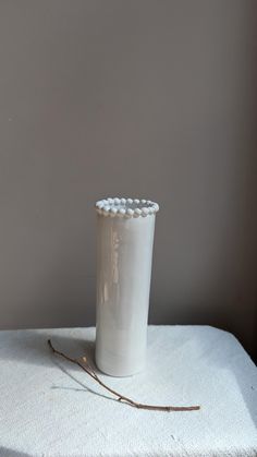 a white vase sitting on top of a table next to a twig and a wall