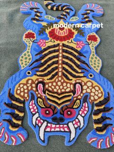 a blue and yellow tiger rug with red flowers on it's head, in the shape of an animal