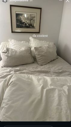 a bed with white sheets and pillows in a bedroom next to a framed photograph on the wall