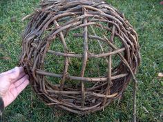 a person is holding a ball made out of branches on the grass with one hand