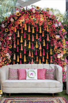 a couch sitting in front of a wall covered with colorful flowers and tassels