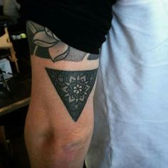 a man with a tattoo on his arm has a black triangle and flowers in it