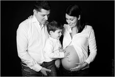 a black and white photo of a pregnant couple with their son, who is holding his belly