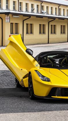 a yellow sports car with its hood open on the street in front of a building