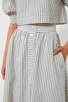 The Linen Stripe Cora Skirt is perfect for countless occasions. Featuring a center button placket detail, side seam pockets, and a side seam zipper, this piece will make you feel elevated and as breezy as the wind by the water. Pair as a matching set with the Linen Stripe Edie Top for an elevated weekend look or with a white top and cardigan for your everyday office outfit. High rise Center button placket detail Side seam pockets Side seam zipper Midi length Unlined A-line Shape Material: 100% L Fitted Summer Skirt With Buttoned Pockets, Spring Midi Bottoms With Button Closure, Relaxed Midi Skirt With Buttons, Chic Skirt With Buttoned Pockets For Spring, Chic Long Skirt With Button Closure, Spring Cotton Skirt With Button Zip Fly, Spring Maxi Skirt With Button Closure In Relaxed Fit, Spring Long Skirt With Buttons, Spring Flared Skirt With Button Closure