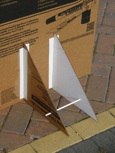 an upside down box on the ground next to a brick sidewalk with two pieces of cardboard sticking out of it