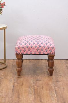 a foot stool sitting on top of a wooden floor next to a vase with flowers