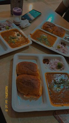 four plates with different types of food on them sitting on a table next to a cell phone