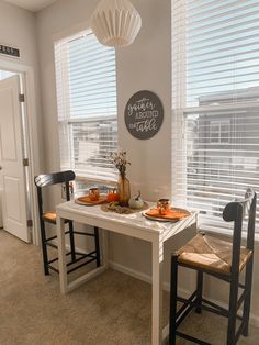 a dining room table with two chairs and a chalkboard sign on the wall above it