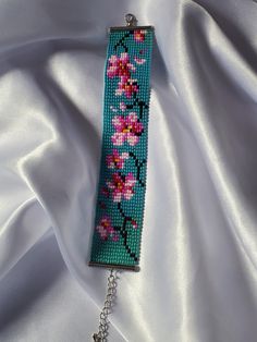 a close up of a key chain on a white cloth with pink flowers and leaves