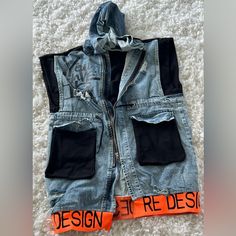 You Will Look Fierce In This Awesome Rdesign Denim Vest. It Features Black Banding On The Top Half Of The Back, The Shoulders And The Pockets. The Bottom Features Bright, Orange Sweatshirt Banding That Says R Design. Drawstring At The Waist. It’s Accented With Some Graphic Writing, And A Snap Off Hood. Made In Turkey, This Brand Is Very Hard To Find In The United States. Urban Denim Vest For Streetwear, Urban Denim Vest For Fall Streetwear, Trendy Black Denim Vest For Streetwear, Studded Leather Vest, Graphic Writing, Orange Sweatshirt, R Design, Jean Jacket Vest, Womens Puffer Vest