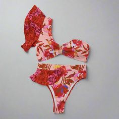 Step into paradise with our Tropical Bloom One-Shoulder Bikini Set. This eye-catching bikini features a vibrant floral print in shades of red, pink, and orange, evoking the beauty of a tropical garden. The one-shoulder top is designed with a stylish ruffle detail, adding a touch of femininity and flair, while the high-waisted bottoms offer a flattering and comfortable fit. Crafted from high-quality polyester and spandex, this bikini set ensures durability and comfort. The quick-drying fabric kee Retro Swimwear, Beachwear Collection, Strapless Bandeau, Bustier Dress, Elegant Dresses Long, Glam Dresses, One Shoulder Tops, Tropical Garden, Cutout Dress