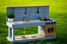 a toy stove and sink in the grass with pots and pans hanging from it