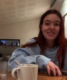 a woman sitting at a table with a cup and cell phone in front of her