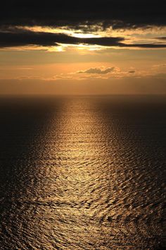 the sun is setting over the ocean as it reflects in the calm water and clouds