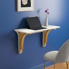 a laptop computer sitting on top of a wooden desk next to a white chair and blue wall