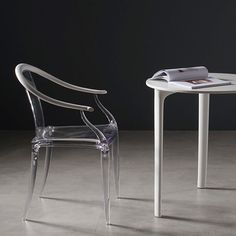 two clear chairs sitting next to each other near a table with a magazine on it