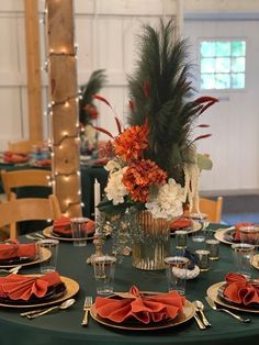 the table is set with orange and white flowers, silverware, and napkins