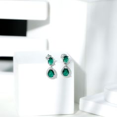 Product Details Class and elegance are truly highlighted in these Created Emerald Earrings which are crafted with exquisite attention to detail. Featuring lustrous 6X8 MM Pear Shaped Lab Emerald that captures the light with every movement. The rich green hue of the Lab Emeralds exudes sophistication and timeless beauty with the 5X7 MM Oval Shape Lab Emerald. To accentuate the center stone is the halo of Moissanite that allows the Lab Emerald to take center stage, while the dangle design adds a t Elegant Hand Set Pear-shaped Earrings, Elegant Hand-set Pear-shaped Earrings, Elegant Moissanite Bridal Earrings With Halo Design, Elegant Emerald Diamond Earrings For Anniversary, Elegant Green Diamond Earrings With Prong Setting, Elegant Green Diamond Earrings In Prong Setting, Green Diamond Chandelier Drop Earrings, Elegant Green Diamond Dangle Earrings, Elegant Green Dangle Diamond Earrings