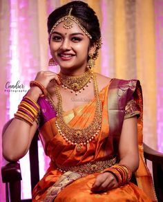 a woman in an orange and gold sari sitting on a chair with her hands behind her head