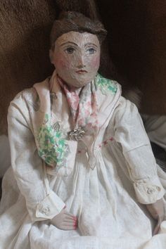 a doll is sitting on the floor wearing a white dress and pink flowered scarf