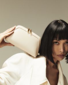 a woman with black hair holding a white purse over her head and looking at the camera